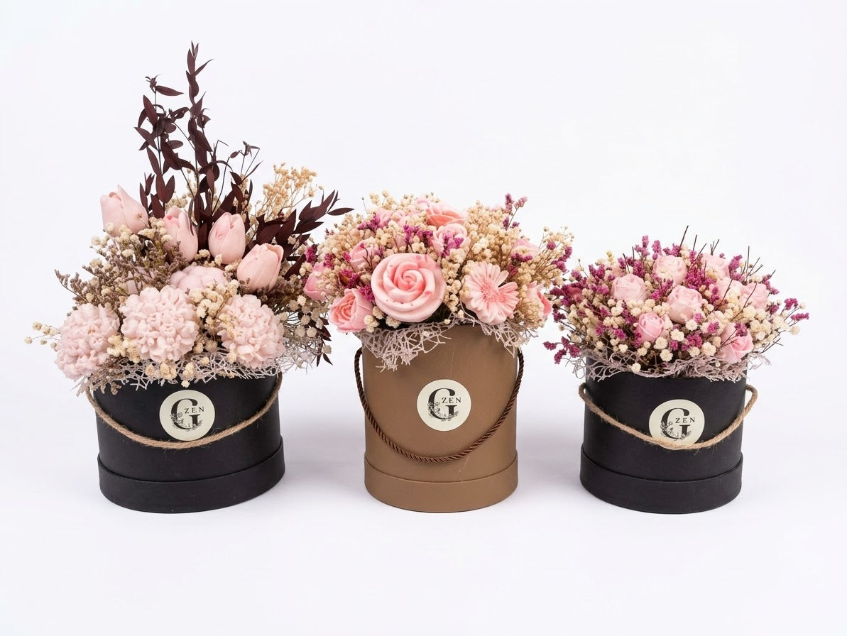 Pink and cream wax flower bouquet with green foliage and burgundy leaves, arranged in a round floral-patterned gift box.