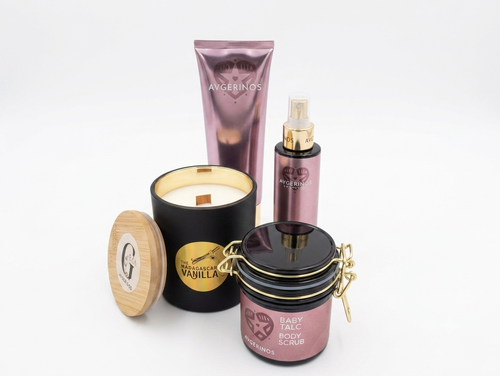 Body care products from Avgerinos Cosmetics on a white background: a vanilla scented candle with wood wick and wooden lid,by Gzen candles,a body scrub in a black jar with gold hardware baby talk, a body & hand cream baby talk in a metallic mauve tube, and a baby talc body oil in a matching mauve spray bottle.
