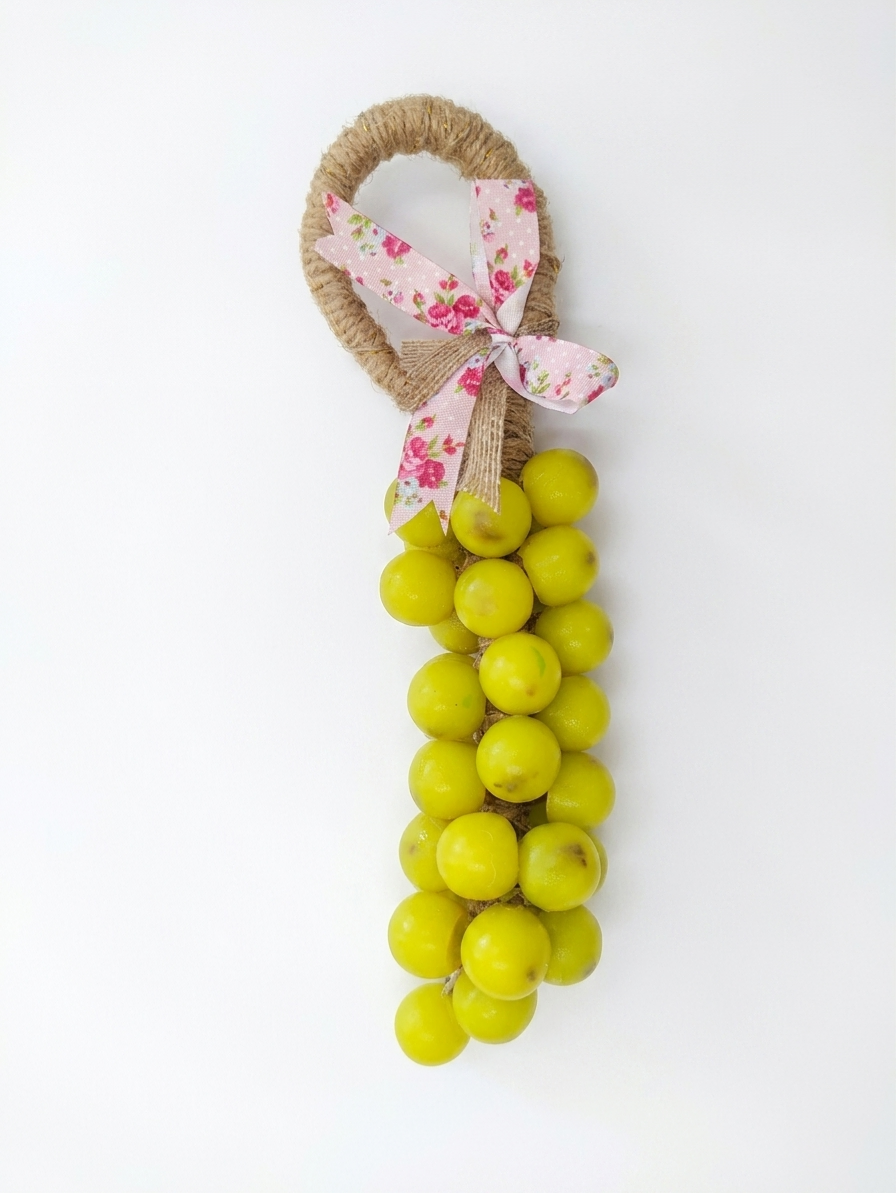 A decorative hanging ornament shaped like a bunch of green soap grapes with a natural jute loop handle, tied with a pink floral ribbon bow, shown on a plain white background.