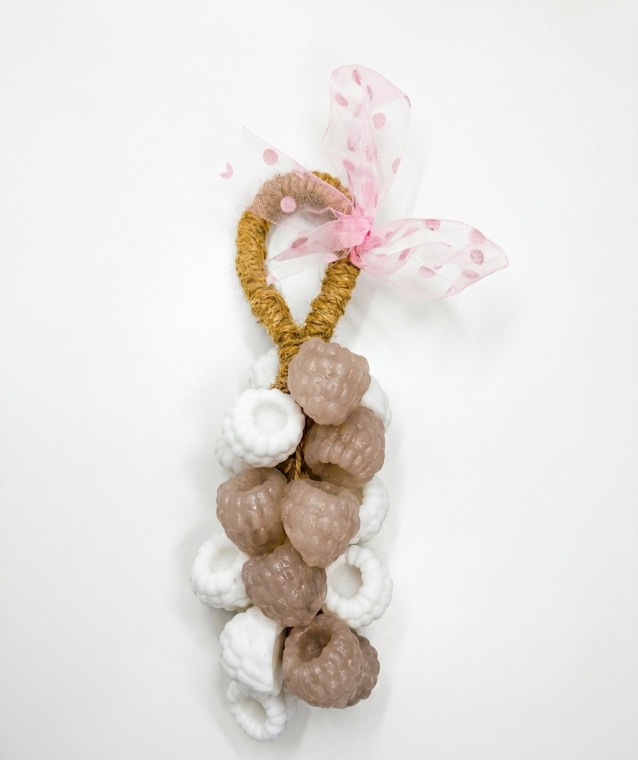 A berries handmade soap on a robe ,or decorative hanging ornament featuring a gold braided loop, white and beige textured donut-shaped charms, and a pink polka-dot tulle ribbon bow, shown on a plain white background.