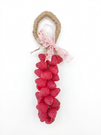 A handmade soap shaped like a bunch of fresh red raspberries, featuring a natural jute-wrapped handle and a pink floral ribbon bow, set against a plain white background.