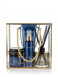 A 4-piece self-care gift set by Avgerinos Cosmetics and Gzen Luxury Candles in a clear acrylic box with a gold frame. The set includes a body scrub jar name star of avgerinos, a body oil bottle, a body cream tube, and a reed diffuser, all in a deep blue color with gold accents, and is accented with a gold rope handle. Perfect for a luxury gift base in Limassol Cyprus. Ship worldwide and to Greece.