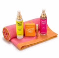 A set of Aygerbino's Summer Addict self-care items arranged on a bright pink and orange towel, including a yellow sunscreen spray, a pink mist spray, a small gold tube, and a yellow glow stick box, on a white background.