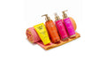A set of four 'Summer Vibes' personal care products from Avgerinos cosmetics including an orange body wash, a pink body wash, a pink hand cream, and a yellow lotion tube, arranged on a wooden tray with a pink towel on a white background.