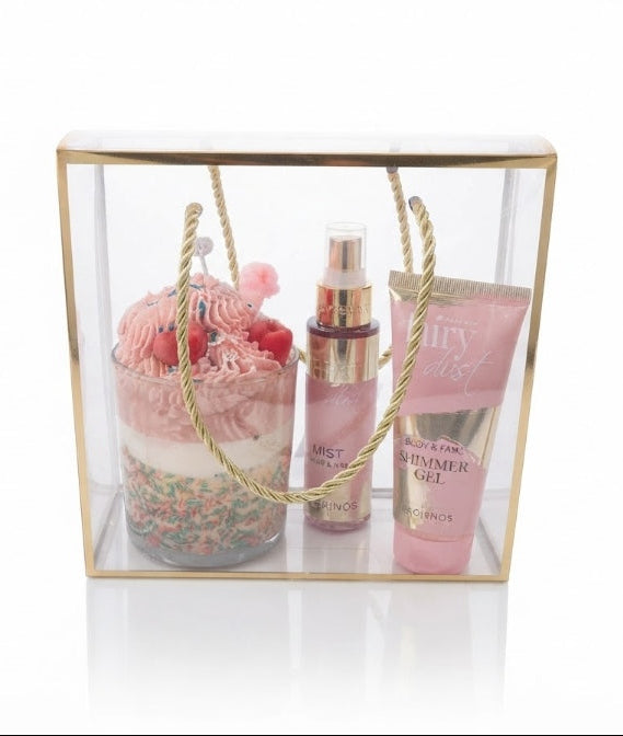 A luxury gift set in a clear acrylic box with a gold frame and rope handles, containing a fairy dust product by avgerinos cosmetics and a whipped desert candle soy on a white background.