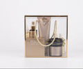 A luxury skincare gift set of avgerinos cosmetics perla  in a clear rectangular box with a gold frame and rope handles. The set includes a tall metallic gold tube, a gold serum bottle, a black jar with a gold lid, and a small gold bottle, all branded with elegant lettering on a clean white background.