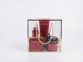 A Hammam by Avgerinos , gift set in a clear acrylic box with a gold frame and rope handle, containing a red body cream, a red body oil bottle, a red body scrub, and a hammam perfume, on a white background.