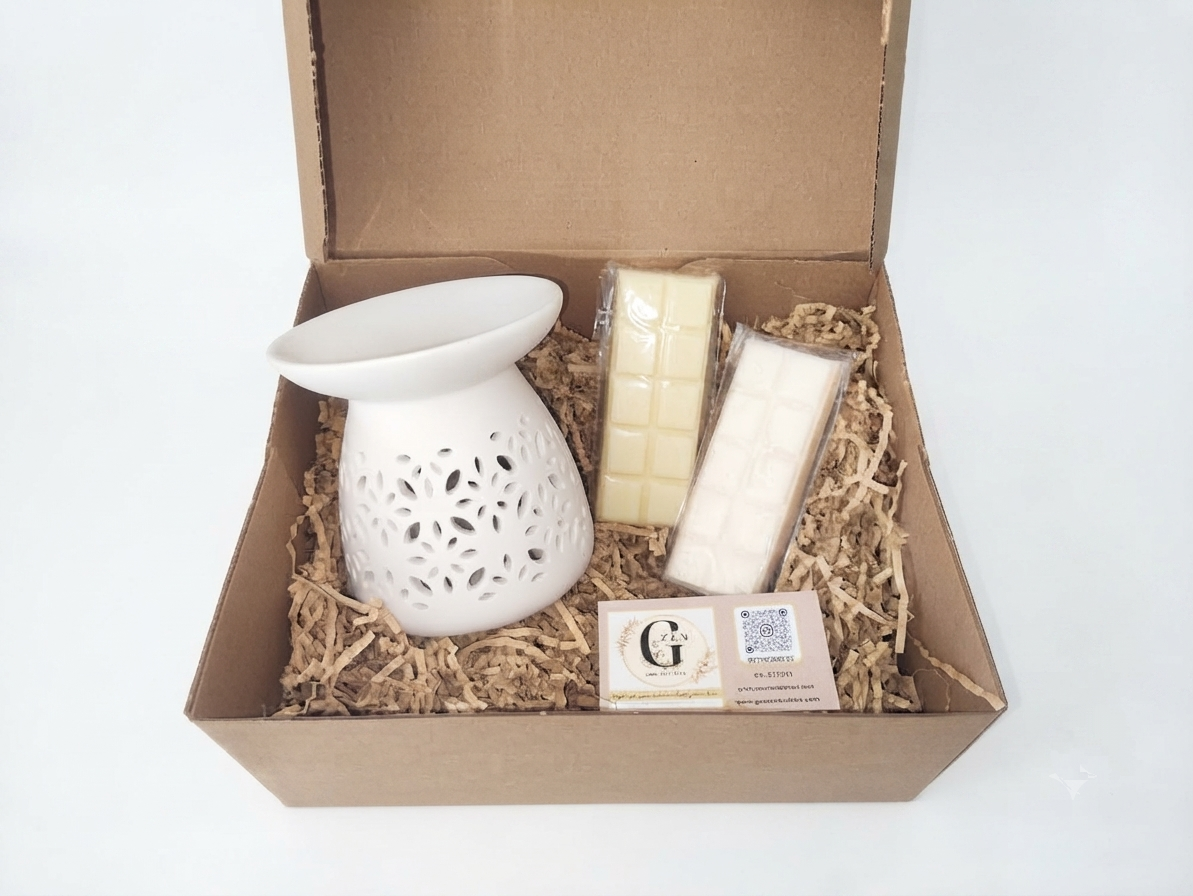 A gift set in a brown cardboard box with shredded paper filler, featuring a white ceramic diffuser, two wrapped cream-colored wax melts, and a branded card.