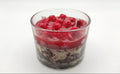 A clear glass candle jar filled with layered dark cookie crumbs, white wax, and a top layer of bright red wax and fresh raspberries, shown on a plain white background.