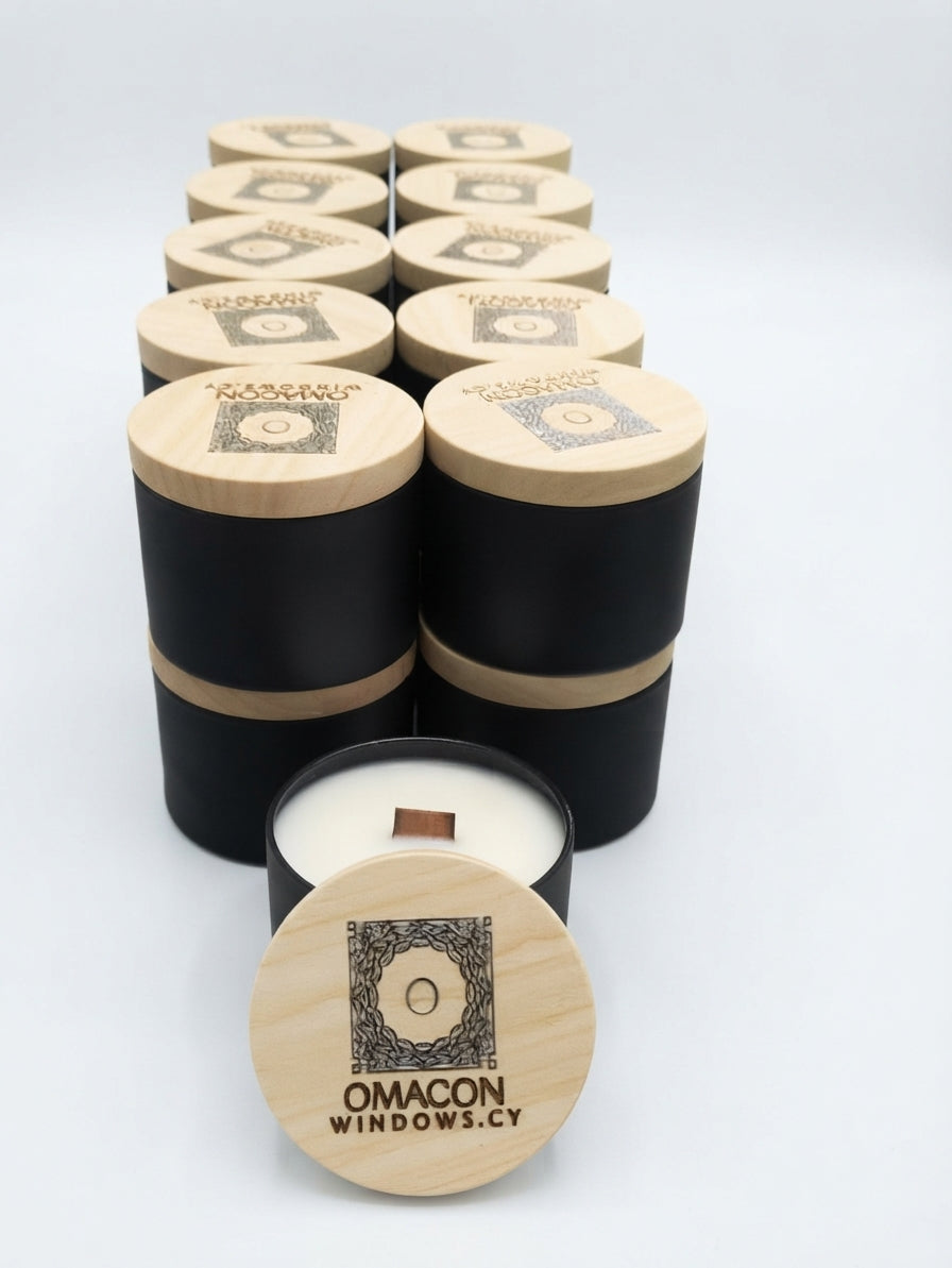 A set of black and light wood cylindrical candle tins arranged on a white background, with one tin open in front showing white wax and a wooden wick. The lids are engraved with a logo and the brand name 'OMACON WINDOWS. gzen candles cooperate gift 