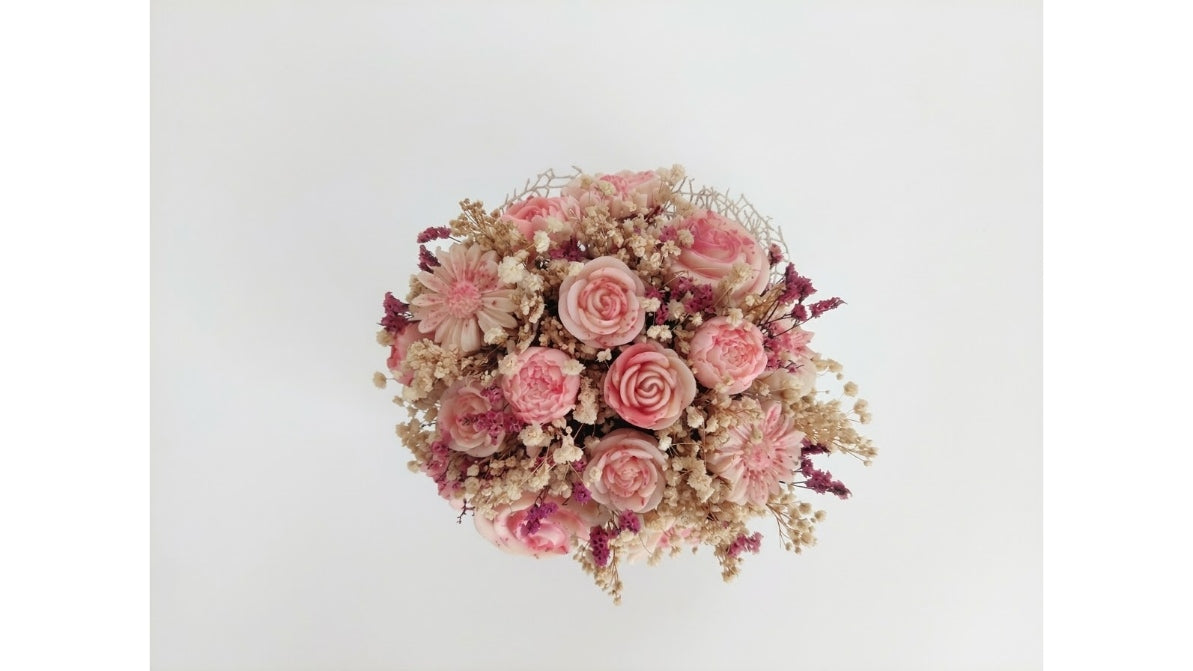 A dried flower bouquet featuring pink roses, pink gerbera daisies, and beige filler flowers, arranged in a round shape against a plain white background.