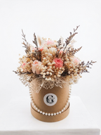 A round kraft paper box filled with dried flowers and botanicals, decorated with a pearl bead garland and a circular white logo sticker that reads 'Glen'. The box sits on a white surface against a clean white background.