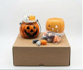 Halloween candy bucket set with a carved jack-o'-lantern bucket, a pumpkin-shaped container, assorted candles and soy wax melts, and a brown cardboard box on a white background. 