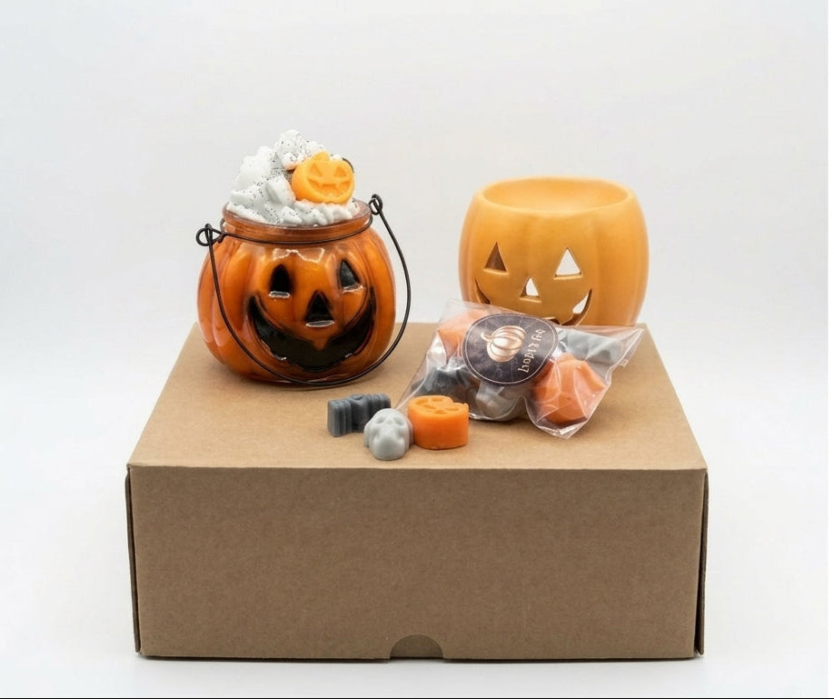 Halloween candy bucket set with a carved jack-o'-lantern bucket, a pumpkin-shaped container, assorted candles and soy wax melts, and a brown cardboard box on a white background. 