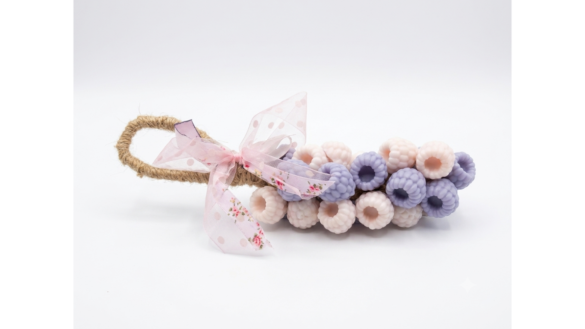 A handmade soap designed to look like a bunch of grapes (berries), featuring light pink and lavender crocheted berries on a tan jute-wrapped stem, adorned with a sheer pink floral ribbon bow, set against a plain white background. Χειροποίητο σαπούνι σε σχήμα σταφύλι Gzen Candles – Αρωματικό δώρο Λεμεσός, Κύπρος