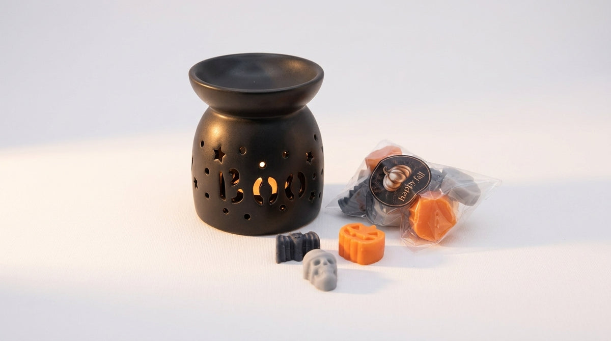 A black ceramic Halloween wax warmer with 'Boo' cut out in the front, shown next to several small wax melts in plastic packaging and loose pieces on a white background.