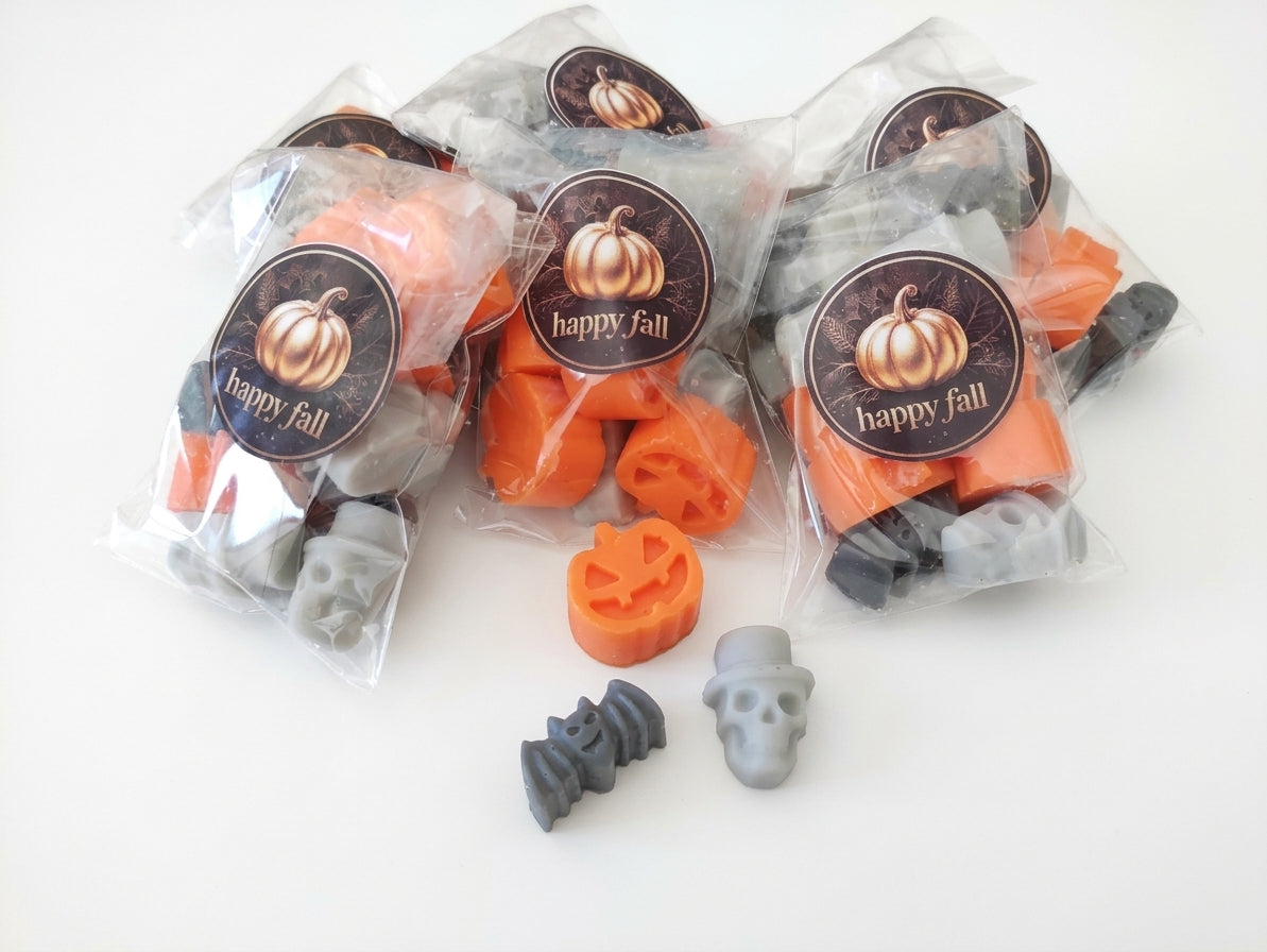 Halloween-themed plastic bags containing orange and gray molded  soy wax melts, with three clear bags in front of a white background and three bags behind showing round 'happy fall' labels.