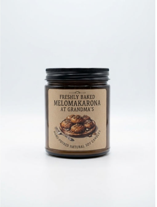 A glass jar candle with a black lid and a tan label reading 'Freshly Baked Melomakarona at Grandma's' on a white background. Scented Christmas candle μελομακορα limassol, cyprus candle