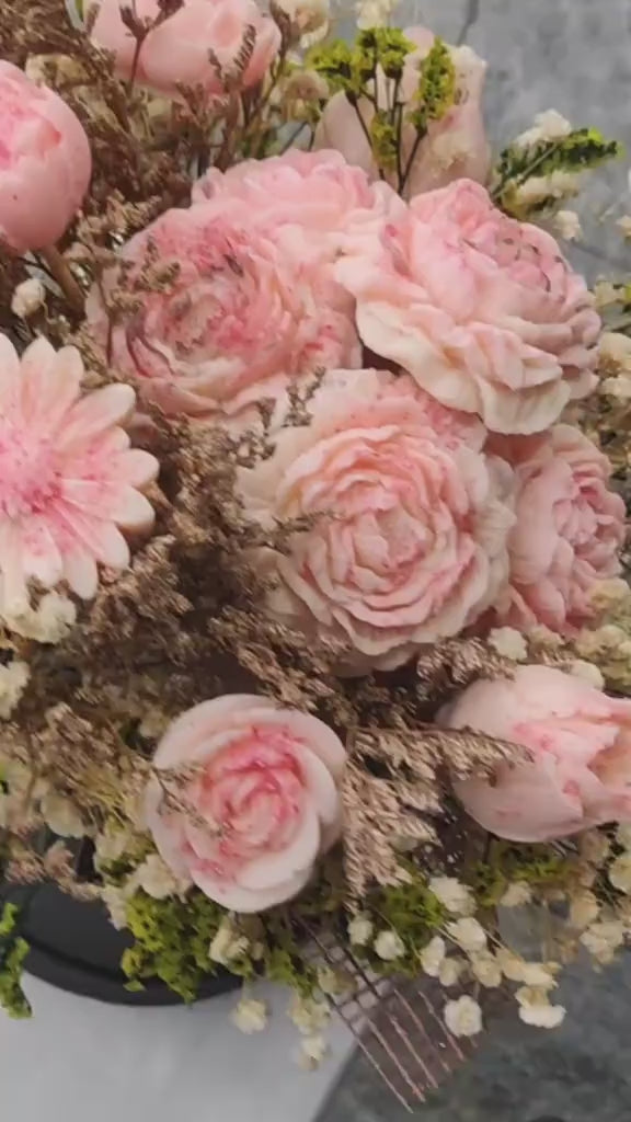 A dried flower bouquet featuring light pink roses, baby's breath, and green foliage, arranged against a plain white background.