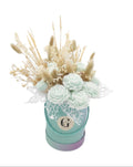 A dried flower arrangement with wax scented flowers in a round pastel box with a monogram 'Gzen' on the front, set against a plain white background.