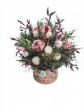 A round floral arrangement featuring pink and white roses, green foliage, and dark burgundy leaves, presented in a decorative round box with a floral pattern, set against a plain white background.