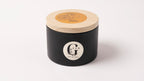 Black metal container with lid featuring a logo of gzen candles on a white background