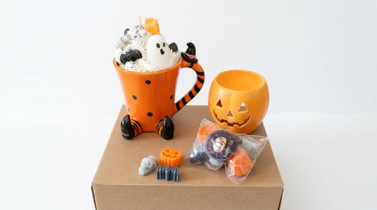 Halloween-themed mug and pumpkin candle set displayed on a brown cardboard box against a white background. The set includes an orange Tigger-shaped mug filled with whipped cream, black polka dots, ghost decorations, and a small pumpkin candle, alongside a jack-o'-lantern-shaped orange candle and small packaged treats.