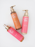Three AVGERINOS Summer Addict body care products from the brand's collection, including a peachy tan spray, a golden yellow body butter, and a pink body mist, arranged on a clean white background.
