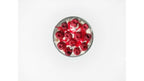 A top-down view of a clear glass bowl filled with white whipped candle  cream and topped with red candle  cherries and red syrup drizzle, set against a plain white background.